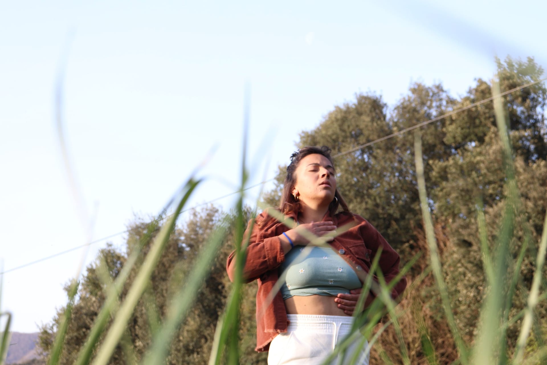 Una mujer entre juncos, con los ojos cerrados y los brazos sobre el pecho, en luz dorada